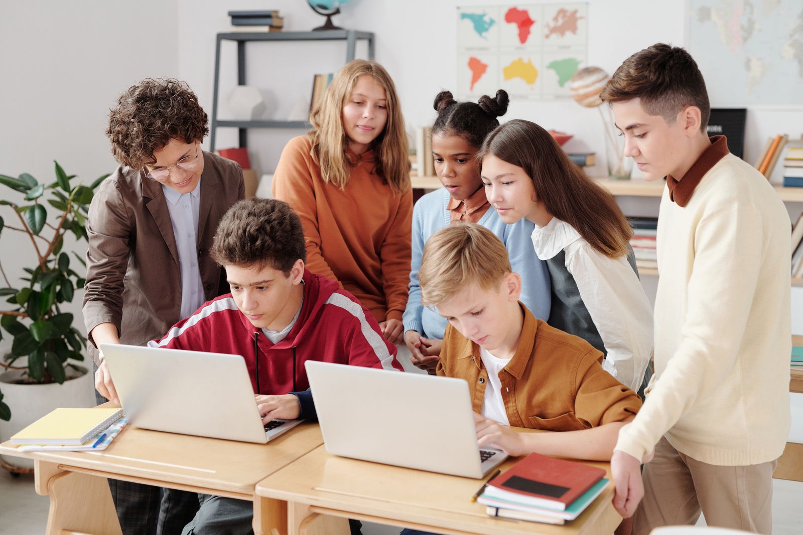 Students gathered around laptops with a teacher in a classroom.