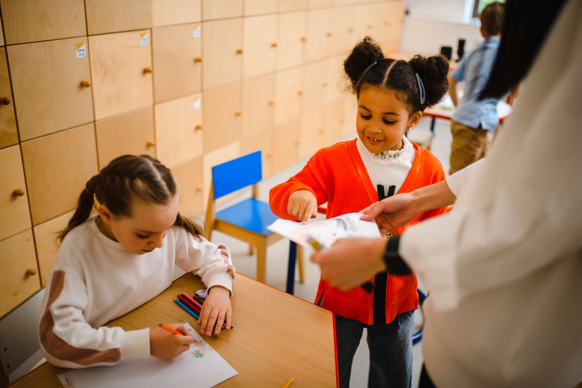 Young students drawing and sharing their work with a teacher.